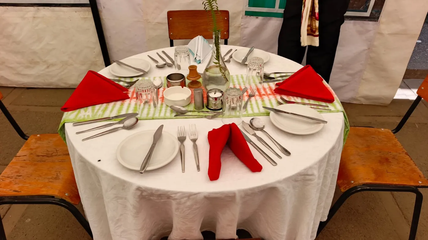 A restaurant table set with white linen, cutlery and red napkins